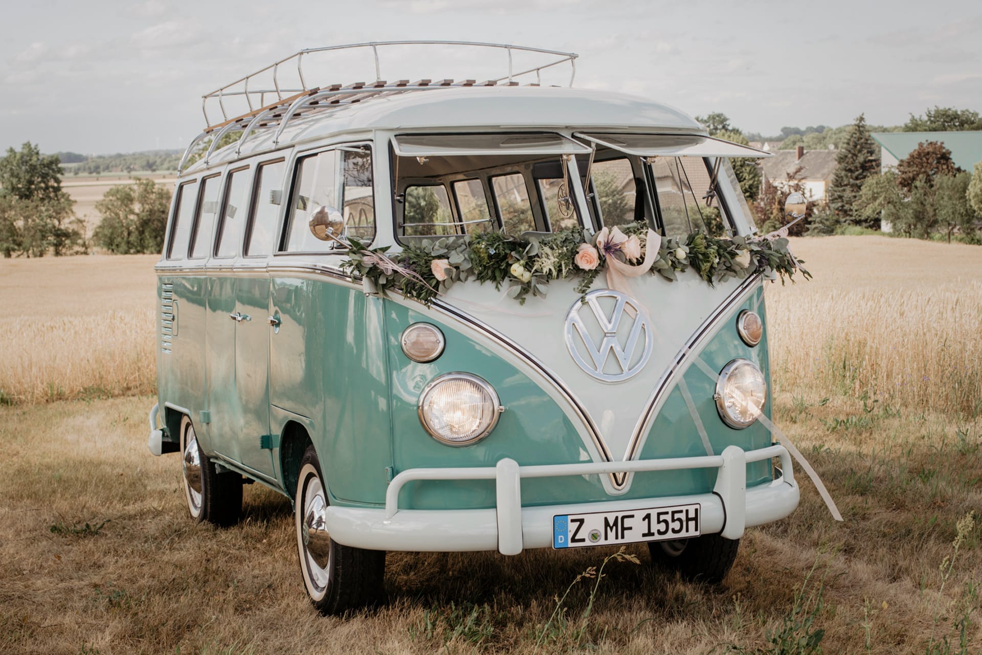 Premium Dekoration Autogirlande Hochzeitsauto quer mit Eukalyptus und rosa Rosen und Schleifen. VW T1 Bus in türkis